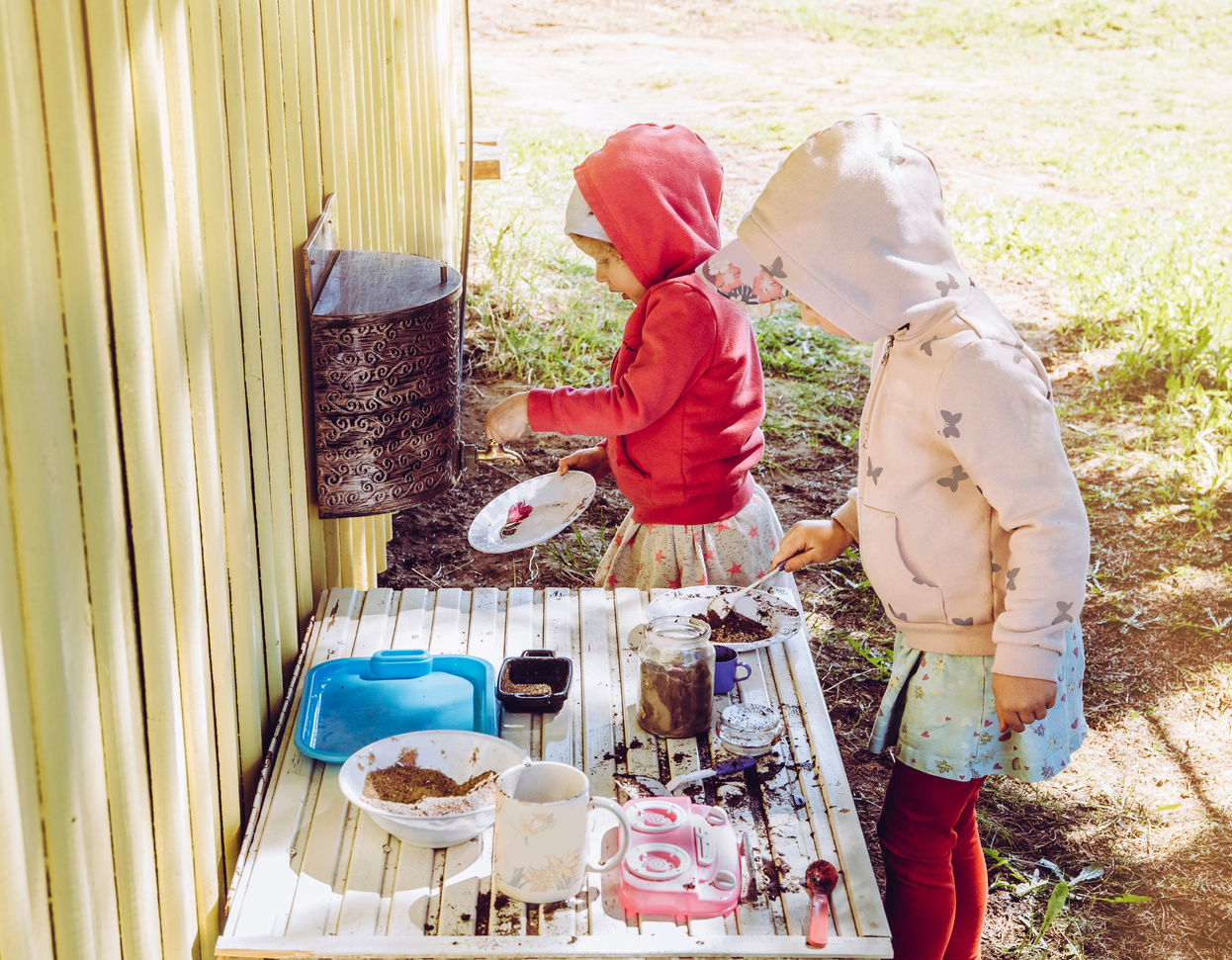 Girls sisters play outdoors in so called mud kitchen.